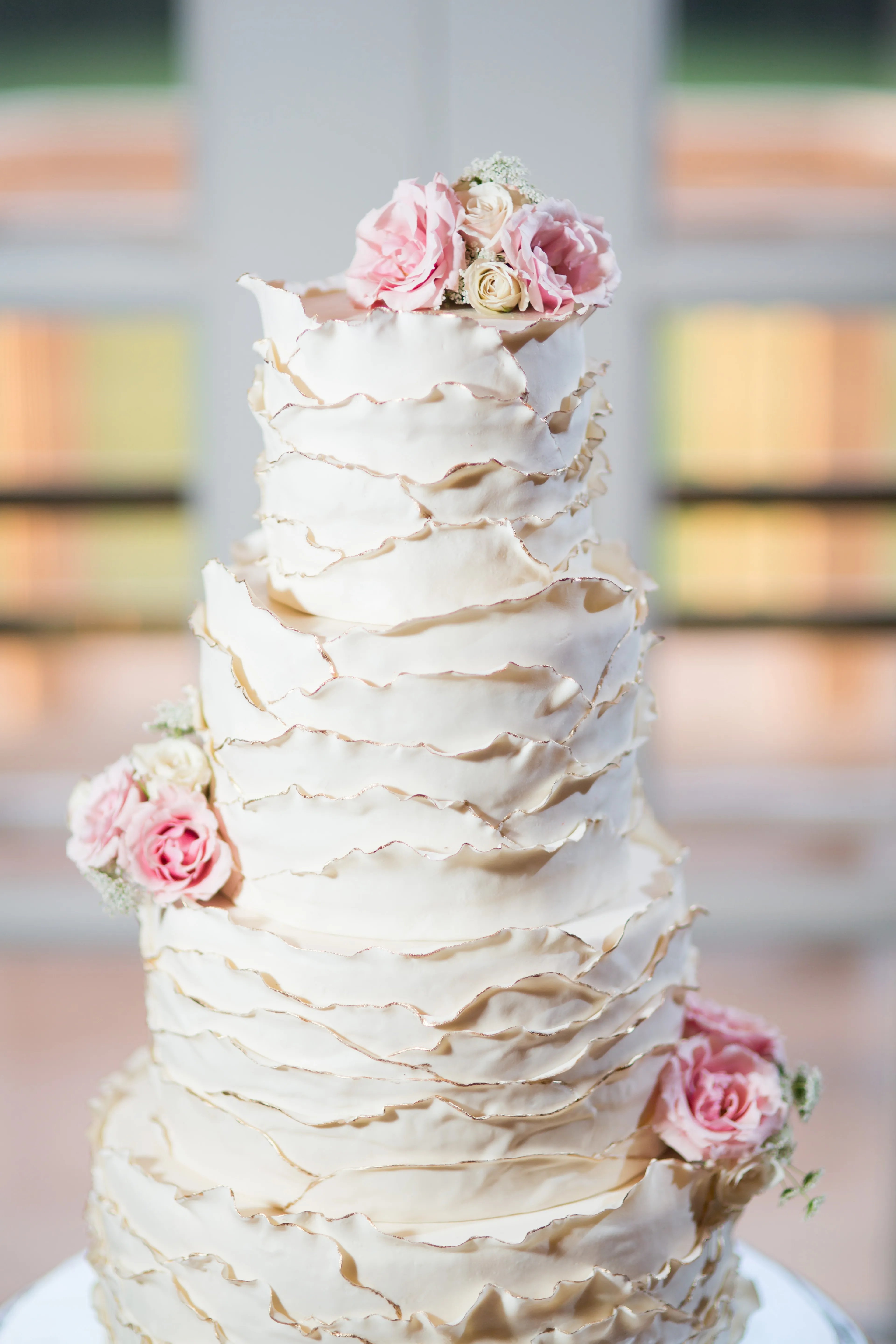 A tall ruffled ivory wedding cake dressed with fresh blush roses