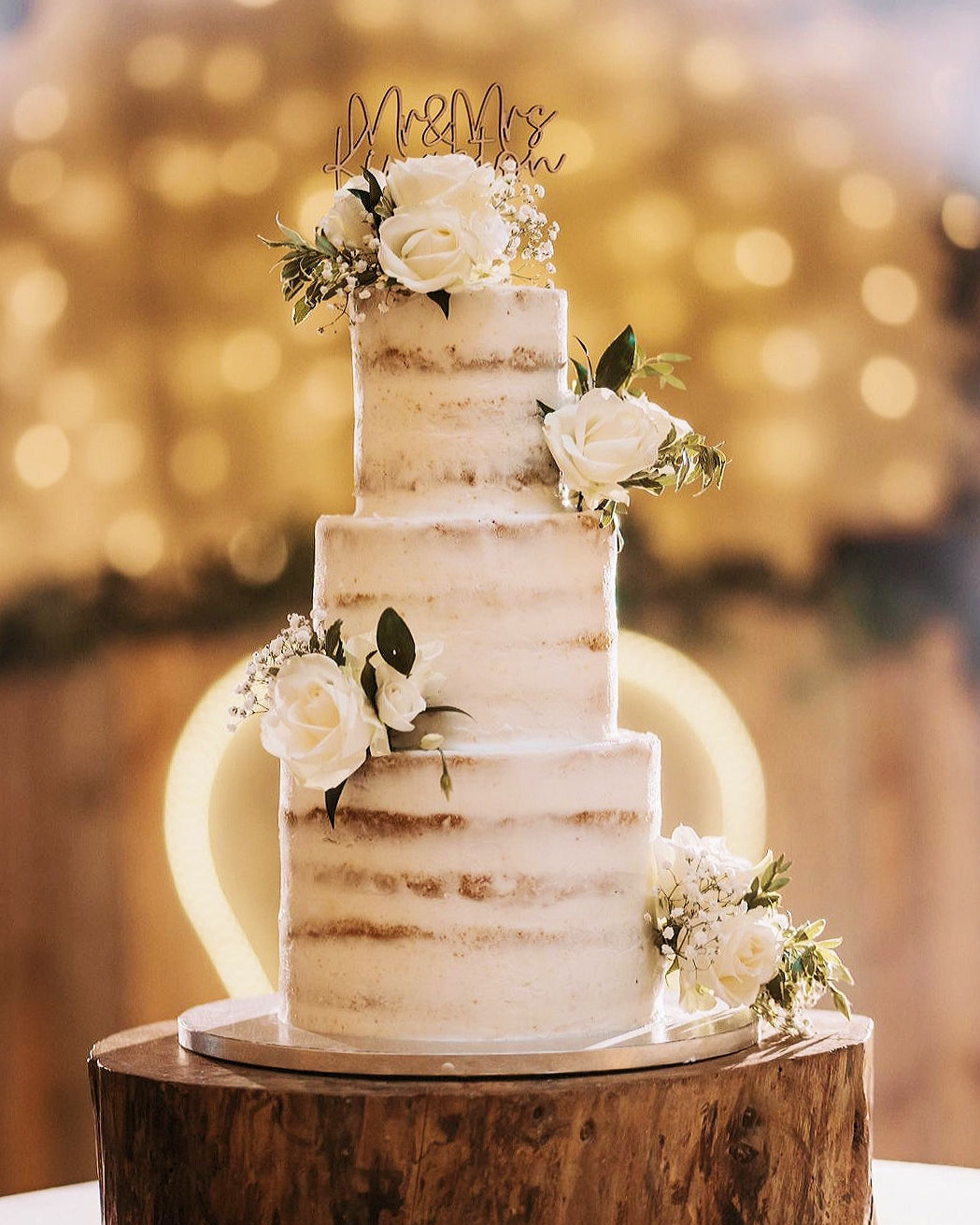 Elegant semi-naked tiered wedding cake dressed with fresh white roses